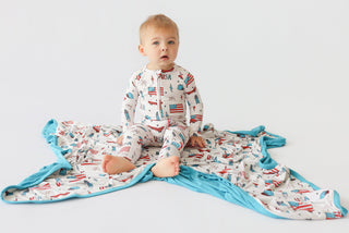 Toddler wearing cream romper with red and blue patriotic prints, paired with turquoise trim and matching blanket.
