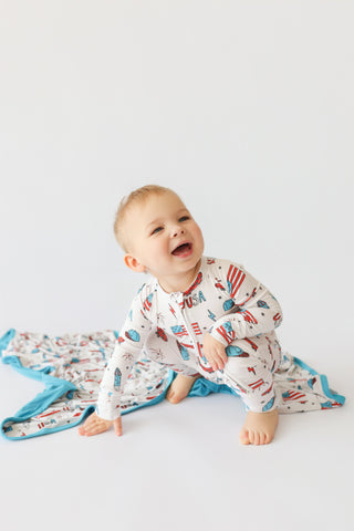 Infant romper with red, white, and blue star and stripe print, featuring blue trim and skating-themed graphics.