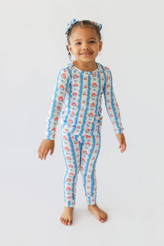 Young child wearing blue and red floral patterned long-sleeve pajamas with matching fabric bows in hair.