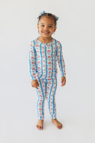 Young child wearing two-piece pajama set with blue and red floral bow print, matching hair bows on top.