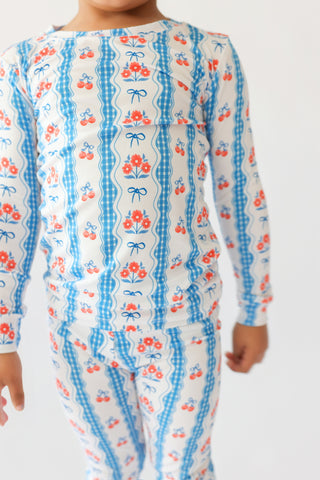 Child wearing long-sleeved pajamas with blue gingham stripes, red flowers, and blue bows on cream background.