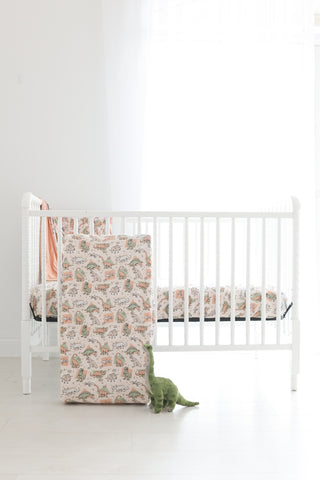 Cream crib sheet with scattered dinosaur print in brown and green tones, displayed on white crib.