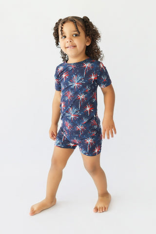 Child wearing navy short-sleeve shirt and shorts with red, white, and blue firework print throughout.