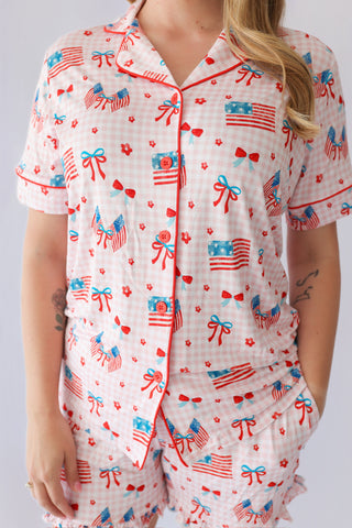Women's short pajama set with pink gingham pattern, red buttons, and red/blue flag and bow print throughout.