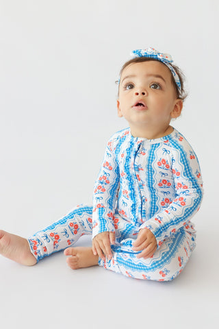 Infant wearing blue and white floral romper with ruffled edges and matching bow headband.