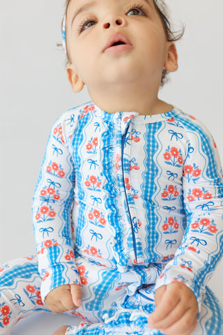 Toddler wearing white romper with blue gingham, red floral, and blue bow print, front snap closure, long sleeves.