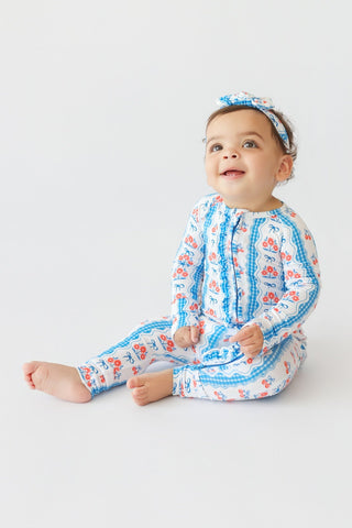 Toddler wearing blue and coral floral print romper with ruffled details and matching headband.