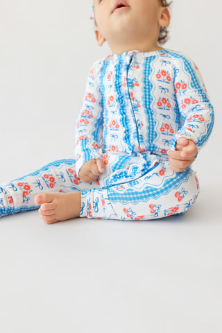 Infant in blue and white romper with red floral print, ruffled trim, and bow details.