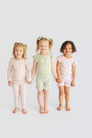 Three children wearing printed short sets in pink gingham, green stripe floral, and coral floral patterns with ruffled sleeve