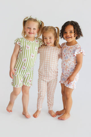 Three children wearing ruffled short sets in green striped, beige gingham, and pink patterned designs.