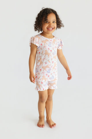 Toddler wearing white short set with ruffled sleeves and boots and flowers print throughout.
