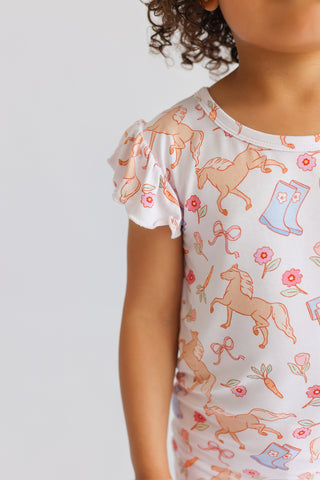 Child's short-sleeved top with ruffled shoulders, cream background with tan horses, pink flowers, blue boots, and bows patter