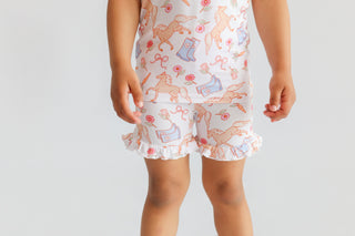 White short set with pink and orange boot and flower print, ruffled leg openings.