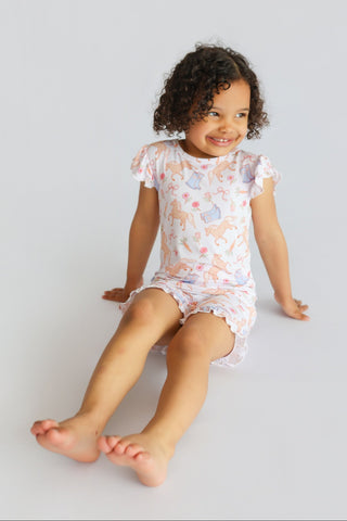 Toddler wearing white short set with boot and floral print, ruffled short sleeves and legs.