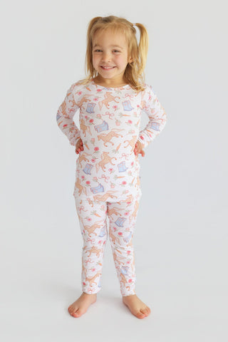 Young child wearing long-sleeved pajama top and pants with boots, flowers, and floral print on cream background.