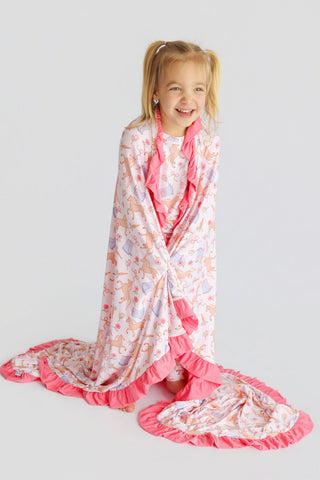Cream blanket with boot and floral print, pink ruffled edges, wrapped around smiling child.