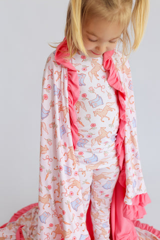 Toddler wearing pink blanket with ruffled edges and boot and flower print pattern.