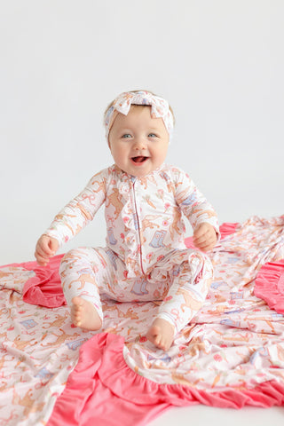 Baby wearing cream romper with boots and floral print pattern, pink ruffled trim, and matching headband.