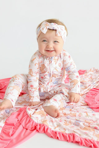 Infant wearing cream romper with pink and orange floral print, matching headband with bow, and pink ruffled trim.