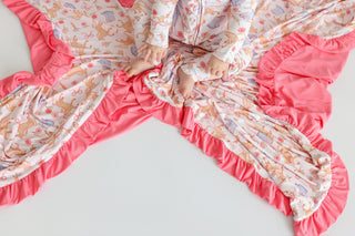 Pink ruffle blanket with cream center featuring boot and floral print, child's hands visible on fabric.