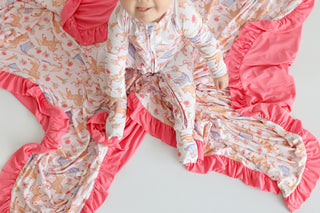 Child wearing cream romper with boot and floral print, bright pink ruffled trim on sleeves and pant legs.