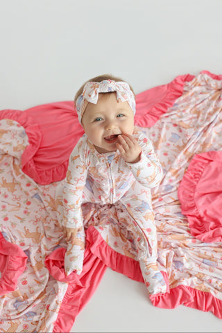 Infant on pink ruffled blanket with boots and floral print pattern, wearing matching outfit and headband.