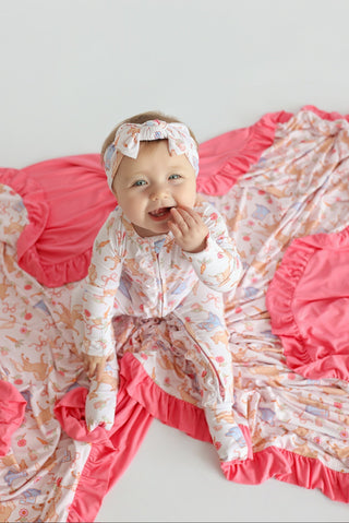Infant wearing cream romper with floral print and long sleeves, paired with matching headband and bright pink ruffled trim.