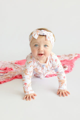 Infant wearing cream romper with floral boot print and matching bow headband, crawling on white surface.