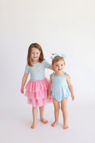 Two young girls wearing tulip-print rompers with ruffled details and matching hair bows.