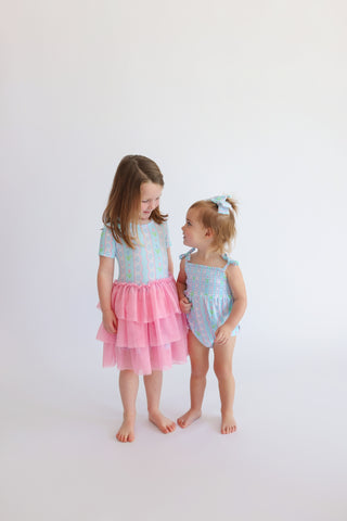 Two young children wearing pastel-colored bubble rompers with tulip print tops and pink tiered skirt bottoms.