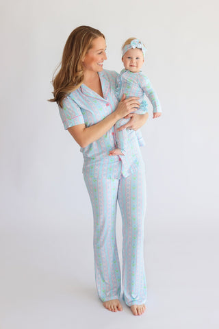 Woman holding infant, both wearing matching light blue rompers with pink and green tulip print and button fronts.