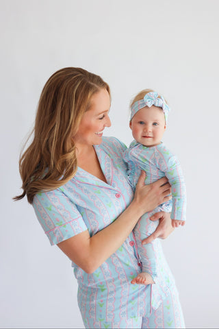 Adult holding infant in matching blue and pink tulip-patterned short-sleeve rompers with ruffled details.
