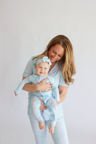 Woman and infant wearing matching multicolored tulip print pajama sets with short sleeves and flare pants, infant wearing coo