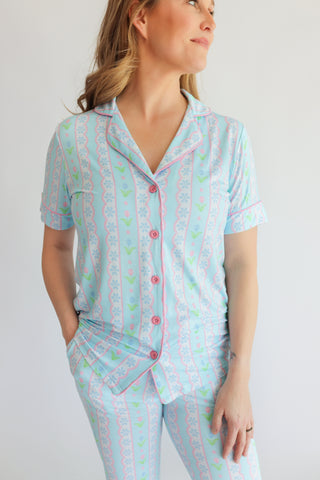 Woman wearing short-sleeve button-up pajama top with tulip and geometric pattern in blue, pink, and green.