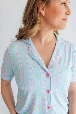 Women's short-sleeve button-up shirt with light blue background, pink and blue geometric pattern, and small tulip print throu