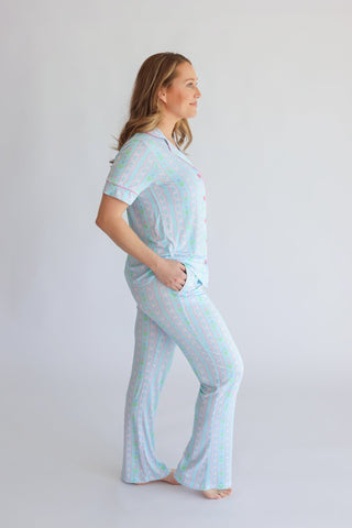 Woman wearing light blue short-sleeve top and flared pants with pink and green tulip pattern throughout.