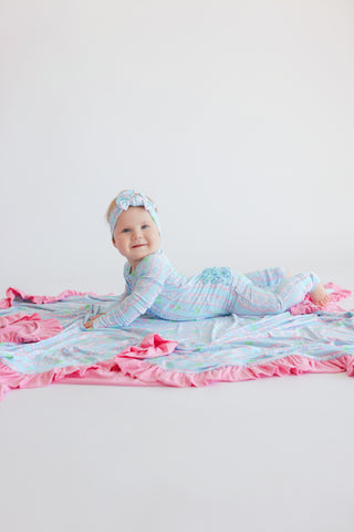 Infant wearing light blue tulip-print romper with pink ruffled trim and matching headwrap, lying on layered fabric.