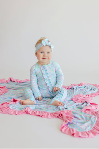 Toddler wearing light blue romper with pastel tulip print and pink ruffled trim, styled with matching headband.