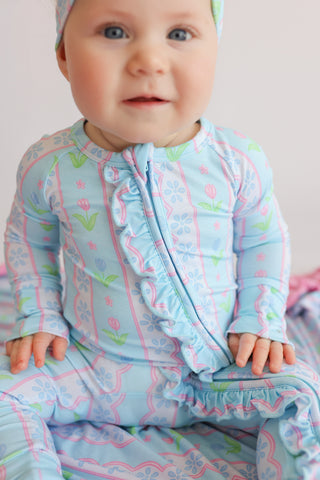 Infant wearing light blue romper with pink tulip and floral print, ruffle front trim, and front zipper closure.
