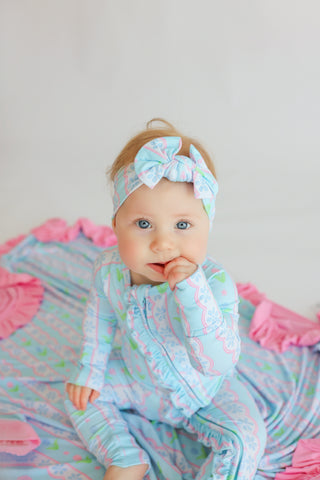 Infant wearing light blue romper with pink tulip print and matching headbow, surrounded by pink ruffled fabric.