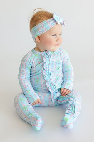 Toddler wearing light blue romper with tulip and geometric print, matching headband with bow, and ruffle trim details.