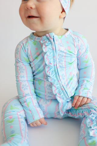 Infant wearing light blue romper with pink tulip and blue flower print, ruffled front closure, and long sleeves.