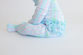 Light blue romper with pink and green tulip print, ruffled hem, and decorative scalloped trim detail.