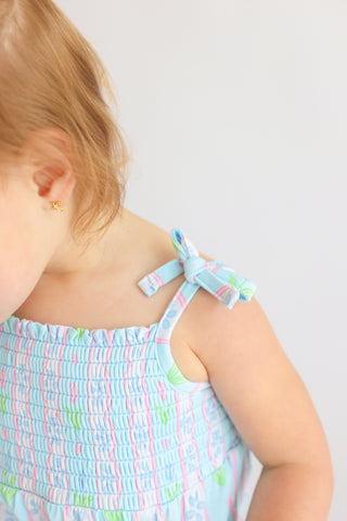 Child wearing light blue romper with pink and green tulip print and tie shoulder straps.