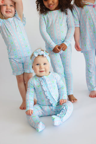 Children wearing light blue rompers with pink and green tulip print and ruffled front panels.