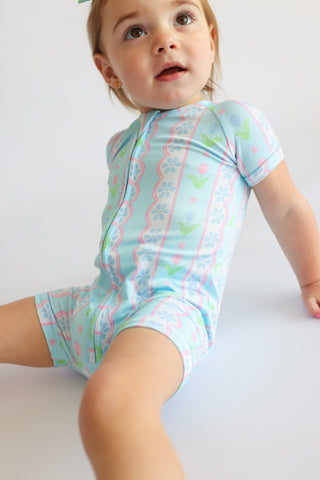 Toddler wearing light blue short-sleeved romper with pink tulip and floral stripe pattern.
