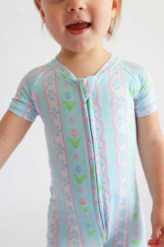 Child's short-sleeve pajama top in light blue with pink tulip and floral stripe pattern and front zipper closure.