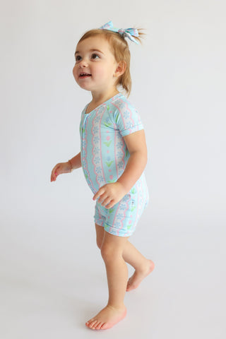 Toddler wearing light blue short-sleeve romper with tulip and geometric print, paired with matching hair clip.