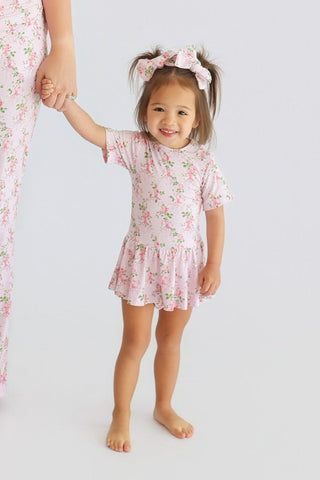 Toddler wearing pink floral bow hair clips in pigtails while holding an adult's hand.