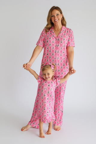 Woman and child wearing matching pink pajama sets with ribbon and bow print pattern.